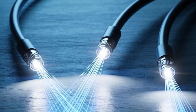 Emitting blue fiber optic cables casting luminescent data beams on dark wood surface