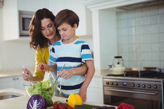 Mother and son are preparing a fresh salad together in a modern kitchen. This image can be used for promoting family bonding, healthy eating habits, parenting tips, and domestic lifestyle content. It is ideal for websites, blogs, and advertisements focusing on family life, nutrition, and home cooking.