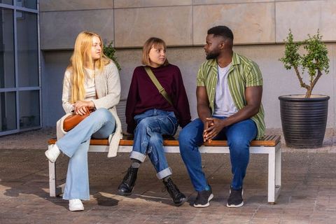 Three friends sitting on bench chatting in city courtyard, casual conversation, relaxed mood