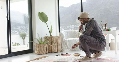 Indian artist painting on floor canvas in sunlit studio with mountain terrace view