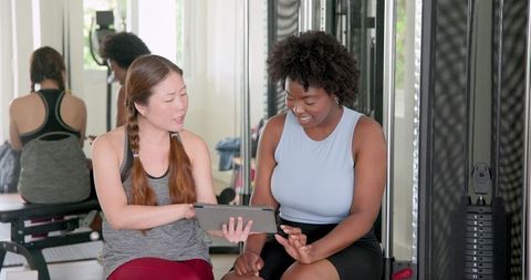 Diverse personal trainer with client using tablet at gym