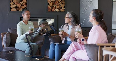 Recording podcast in cozy living room with women chatting, holding drinks and microphones