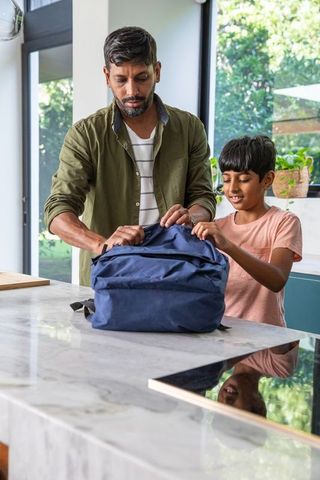 Father and son packing backpack together in modern kitchen