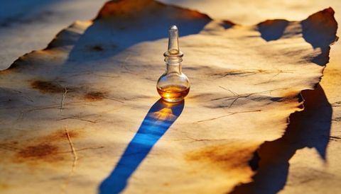 Amber glass vial casting long blue shadow over burnt parchment bathed in golden light