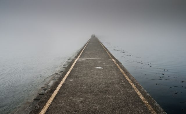 The long concrete pathway disappears into the thick fog, creating a mysterious and tranquil scene over a calm ocean. The image evokes a sense of serenity, calmness, and the endless possibilities beyond the horizon. It is suitable for themes of solitude, journey, tranquility, and can be used for backgrounds, web design, inspirational posters, and more.
