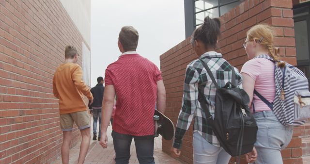 Group of teenagers walks together towards school campus, carrying backpacks. Ideal for educational materials, back-to-school promotions, and youth-oriented advertising campaigns.