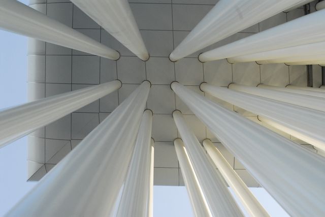 This view of white columns reaching up to a modern tiled ceiling gives a unique perspective on contemporary architecture. The symmetrical and abstract composition can be used in themes related to architectural design, construction, urban planning, and artistic photography projects. Ideal for promoting modern building techniques or for decoration in modern spaces.