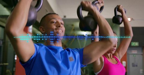 Fitness duo pressing kettlebells overhead wearing blue shirt and pink tank with hud overlay