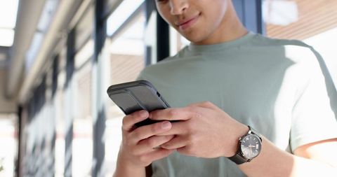 Smiling young man checking smartphone in modern corridor