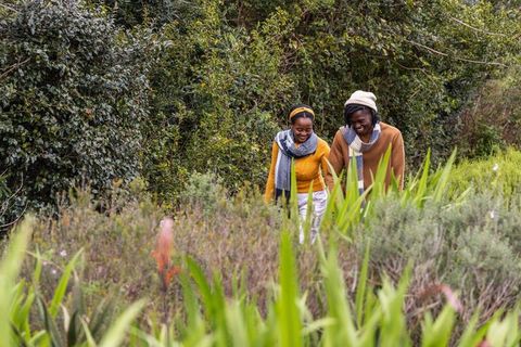 Two african american women walking lush garden path wearing cozy knit sweaters, scarves