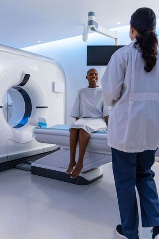 African american woman sitting on ct scanner smiling while technologist preparing radiology exam