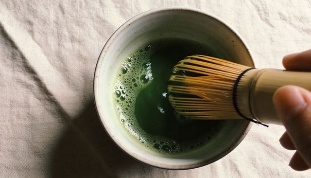 Hand-whisking vibrant matcha in ceramic bowl with bamboo chasen over beige linen cloth
