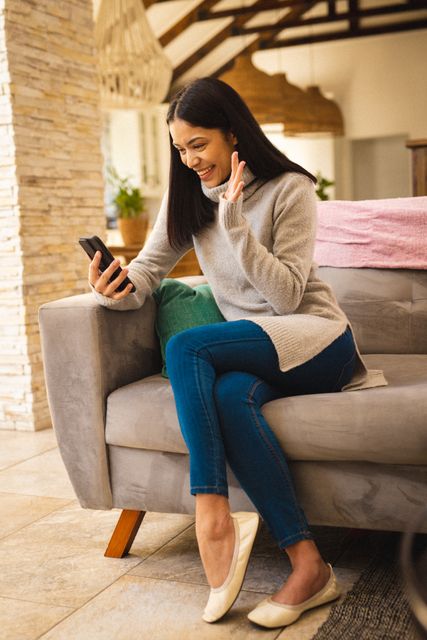 Biracial woman smiling and using smartphone in living room. Spending quality time at home and lifestyle concept.