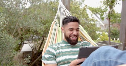Man Relaxing on Hammock Patio with Tablet Surrounded by Nature