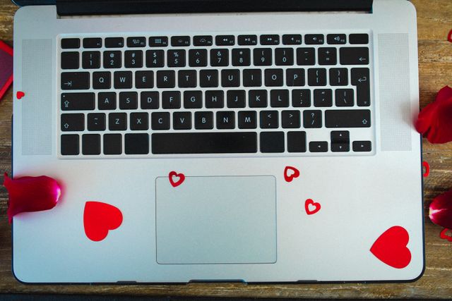 This image shows a laptop on a wooden table, adorned with rose petals and heart shapes. It is perfect for illustrating themes of love and technology, romantic gestures, or Valentine's Day. It can be used in articles, blogs, or advertisements related to digital romance, online dating, or work-life balance.