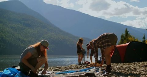 Group of Friends Setting Up Campsite by Mountain Lake