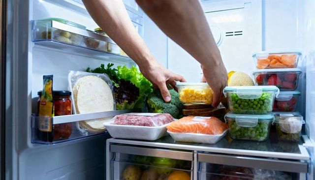 Hands reaching into fridge grabbing prepared corn cup among meal prep containers