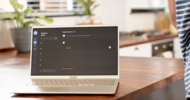 Person interacting with AI chatbot on a laptop in casual home kitchen. Ideal for illustrating home office environments, advancements in AI technology for home use, smart home integrations, and remote work lifestyle.