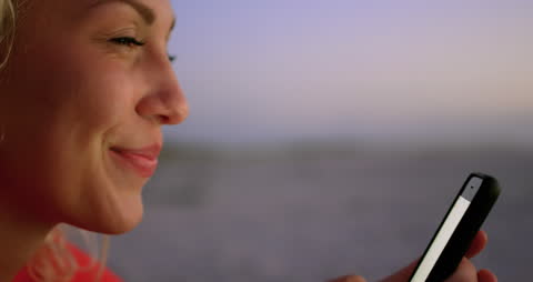 Young Woman Smiling While Using Phone at Beach Sunset
