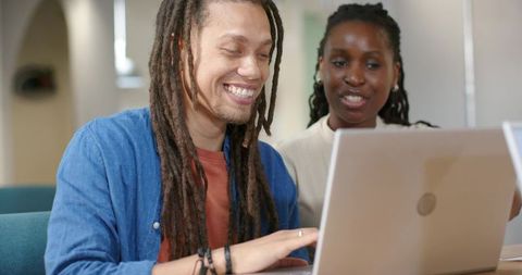 Smiling African American students collaborating on laptop in modern classroom environment