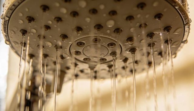 Closeup chrome shower head spraying thin streams with droplets, modern bathroom fixture