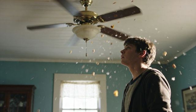 Teen watching ceiling fan scattering dust and debris in sunlit teal room