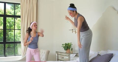 Diverse friends toasting champagne in sunlit bedroom during pajama spa party