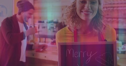 Smiling Barista Holding Merry Sign in Cozy Cafe