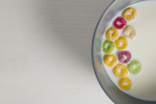 Overhead view of a bowl of milk with colorful cereal rings on a white background. Ideal for use in breakfast-themed advertisements, healthy eating campaigns, or food blogs. Perfect for illustrating morning routines or nutritional content.