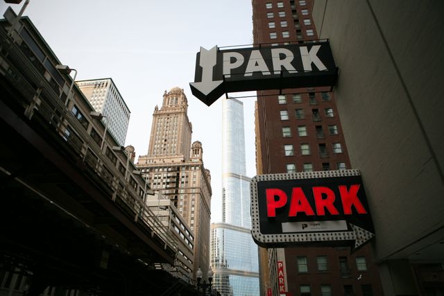 This image captures an urban street view with various high-rise buildings and prominent parking signs. It contrasts modern skyscrapers with older architectural styles, showcasing the busy and bustling atmosphere of a city downtown. This picture is ideal for illustrating urban themes, highlighting city infrastructure, or being used in architectural features and travel blogs focused on metropolitan experiences.