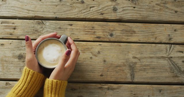 Person holding warm coffee on a rustic wooden table, perfect for illustrating concepts of relaxation, cozy mornings, autumn vibes, and rustic settings. Ideal for use in blogs about coffee culture, morning routines, or cozy lifestyles.