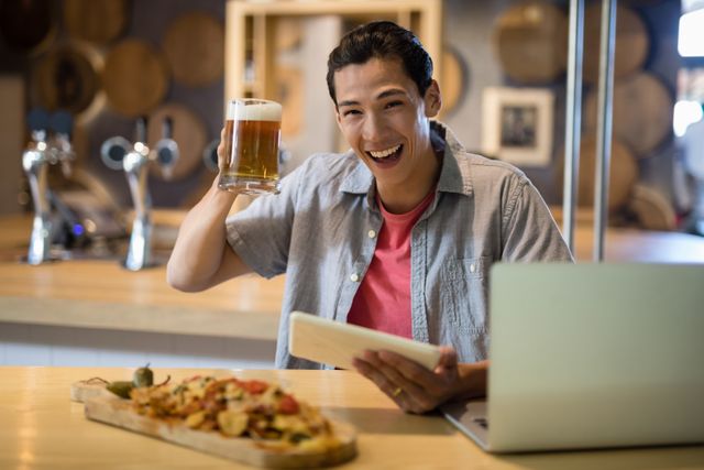 Portrait of smiling man holding beer mug and digital tablet in restaurant