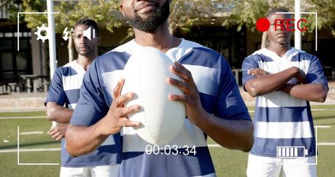 Rugby center holding ball with teammates standing on sunlit field and rec overlay