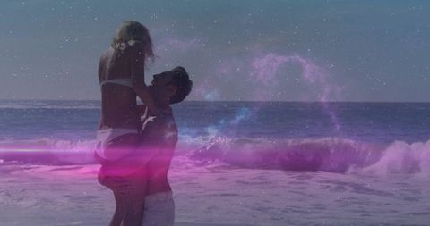 Couple lifting and embracing on beach with dreamy purple light and ocean waves