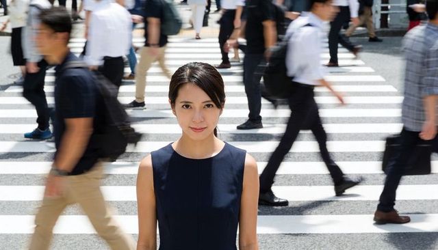 Focused businesswoman standing on busy scramble crosswalk with commuters rushing by