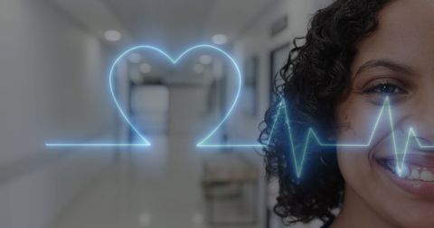 Smiling female doctor with heartbeat monitor overlay in hospital hallway