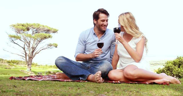 A Caucasian couple enjoys a romantic picnic with wine in a scenic outdoor setting, with copy space. Their cheerful interaction and relaxed posture suggest a moment of leisure and connection amidst nature.