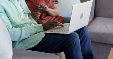 Senior couple making online payment on laptop while sitting on living room sofa