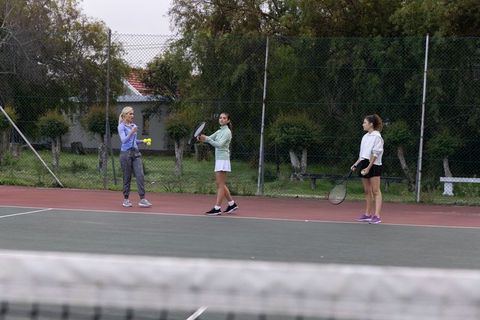 Women practicing tennis at baseline on outdoor court with coach tossing balls