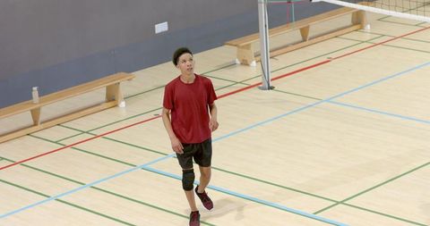 African american teen training volleyball in gymnasium wearing knee support and red shirt