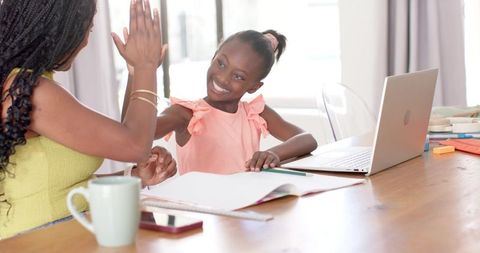 Smiling mother and daughter high-fiving during homework and online learning at home