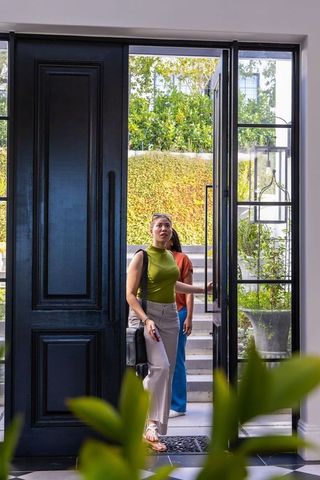 African american women entering modern home through black door into sunlit courtyard