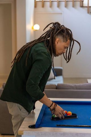 African american man arranging pool balls on blue billiard table in modern living room