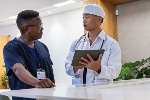 Black and asian doctors reviewing tablet at clinic reception collaborating on patient care