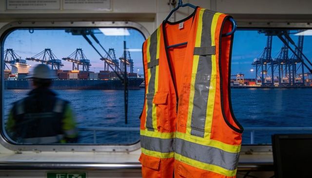 Hi-vis safety vest hanging on vessel bridge with container cranes at dusk harbor