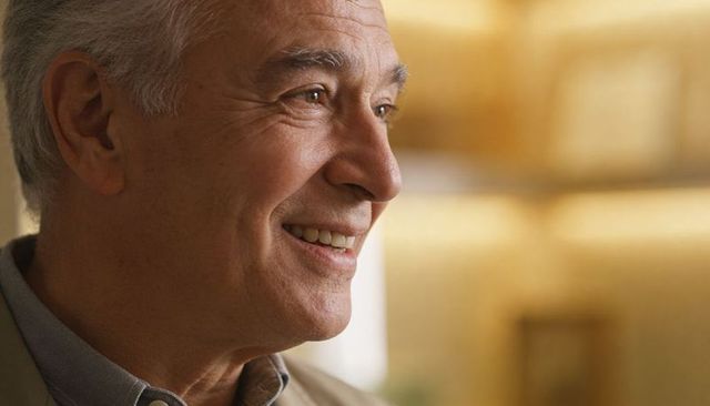 Smiling senior man wearing collared shirt and blazer enjoying warm interior light with gentle optimi
