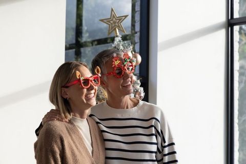 Two generations wearing festive red glitter glasses beside decorated christmas tree smiling