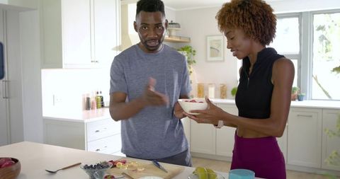 African american couple preparing colorful fruit bowl at bright modern kitchen island