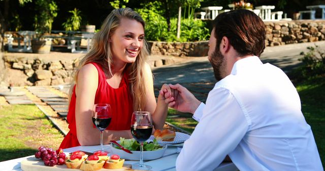 A young Caucasian couple enjoys a romantic outdoor meal, with copy space. They share a moment of connection over wine and food in a serene garden setting.