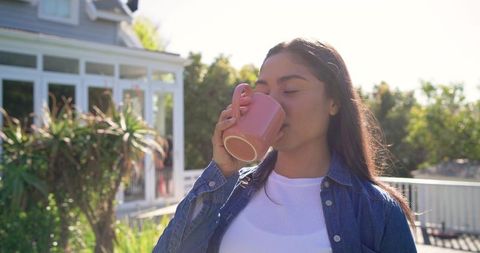 Young woman sipping from pink mug on sunny deck morning relaxation outdoor lifestyle
